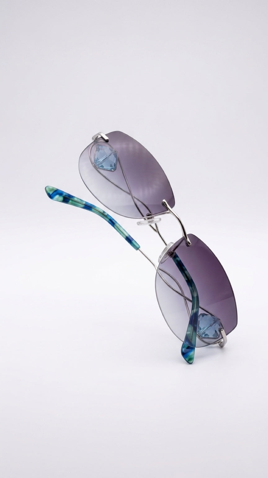 Rimless sunglasses with oval purple-tinted lenses and tortoiseshell-patterned blue and green arms on a light gray background.