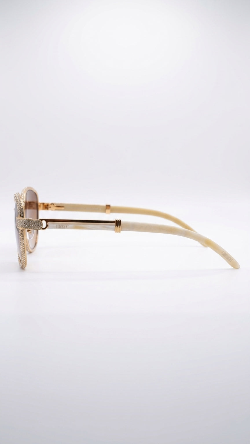 A pair of designer sunglasses shown in profile on a clean white background. The frames feature a textured gold-tone metal with a prominent diamond-encrusted front and matching diamond-embellished temples.