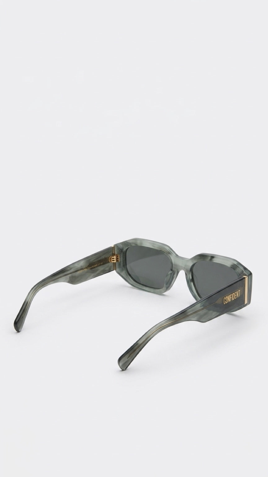 Oversized square sunglasses with a translucent smoky green acetate frame and dark gray lenses, featuring gold-tone metal hinges and the brand name 'GEMSTAR' printed in gold on the temple.