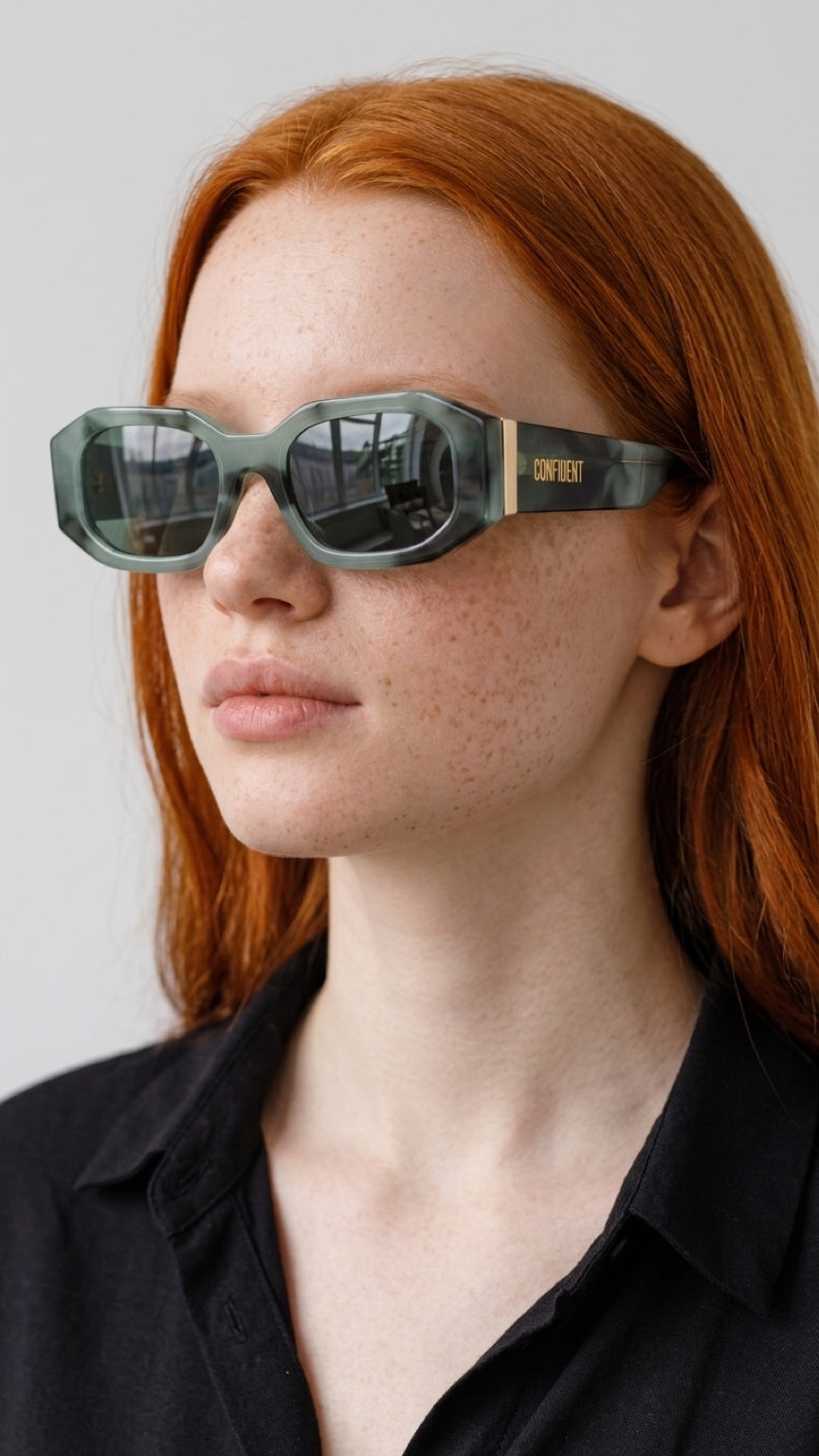 A close-up of a model with red hair wearing geometric square CONFILVARO Sage Green Marble-Effect Rectangle Sunglasses with a translucent sage green frame and gold accents on the temples.