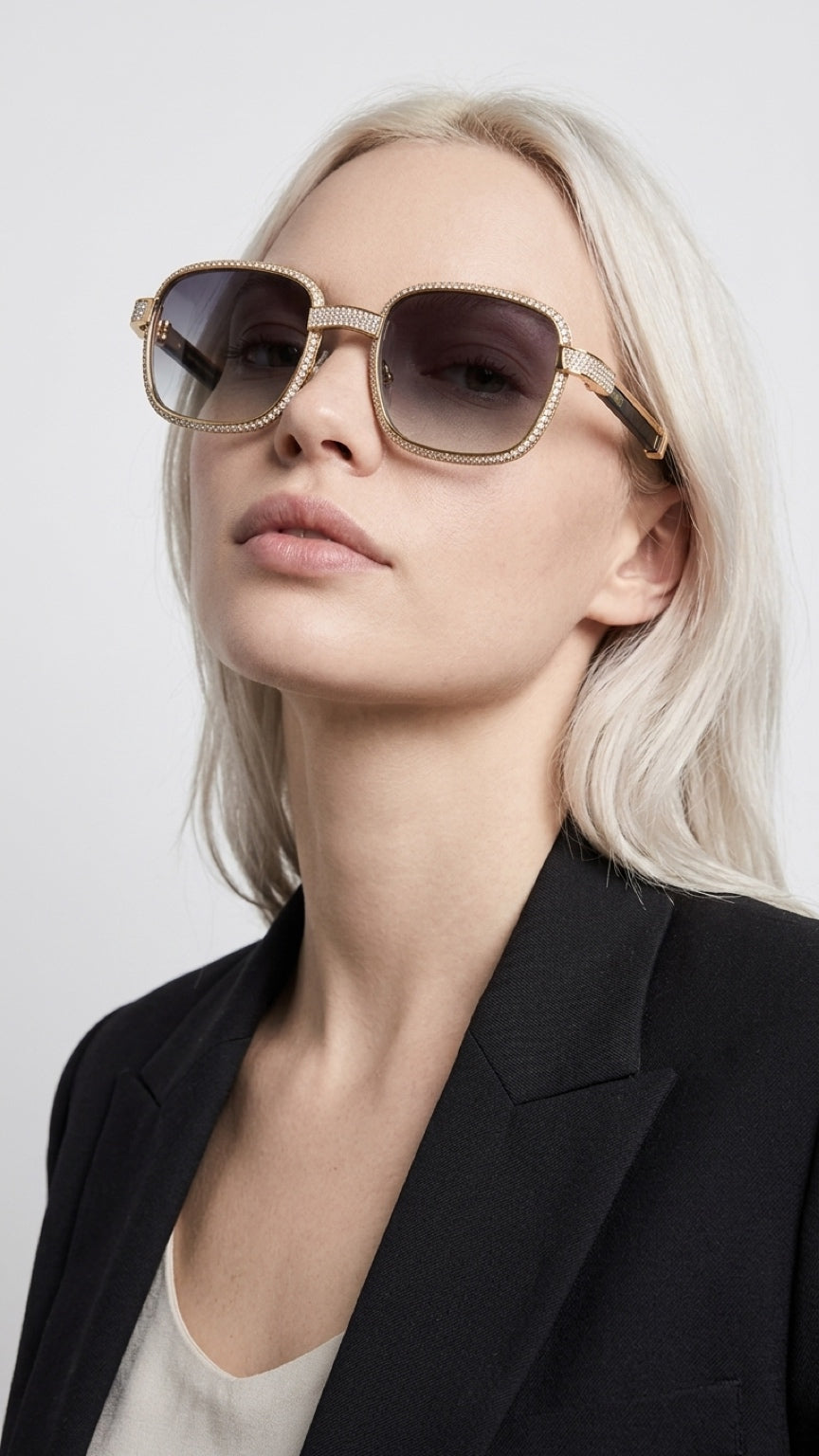 A close-up of a blonde woman wearing oversized square sunglasses with a gold-tone metal frame and dark lenses, paired with a black blazer.