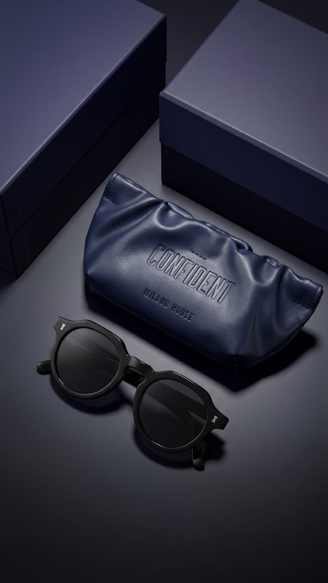 Black round-frame sunglasses with dark lenses displayed next to a navy blue satin glasses case embossed with the brand name 'CONFIDENT' and 'PALAIS ROUGE', set against a dark navy background with matching product boxes.