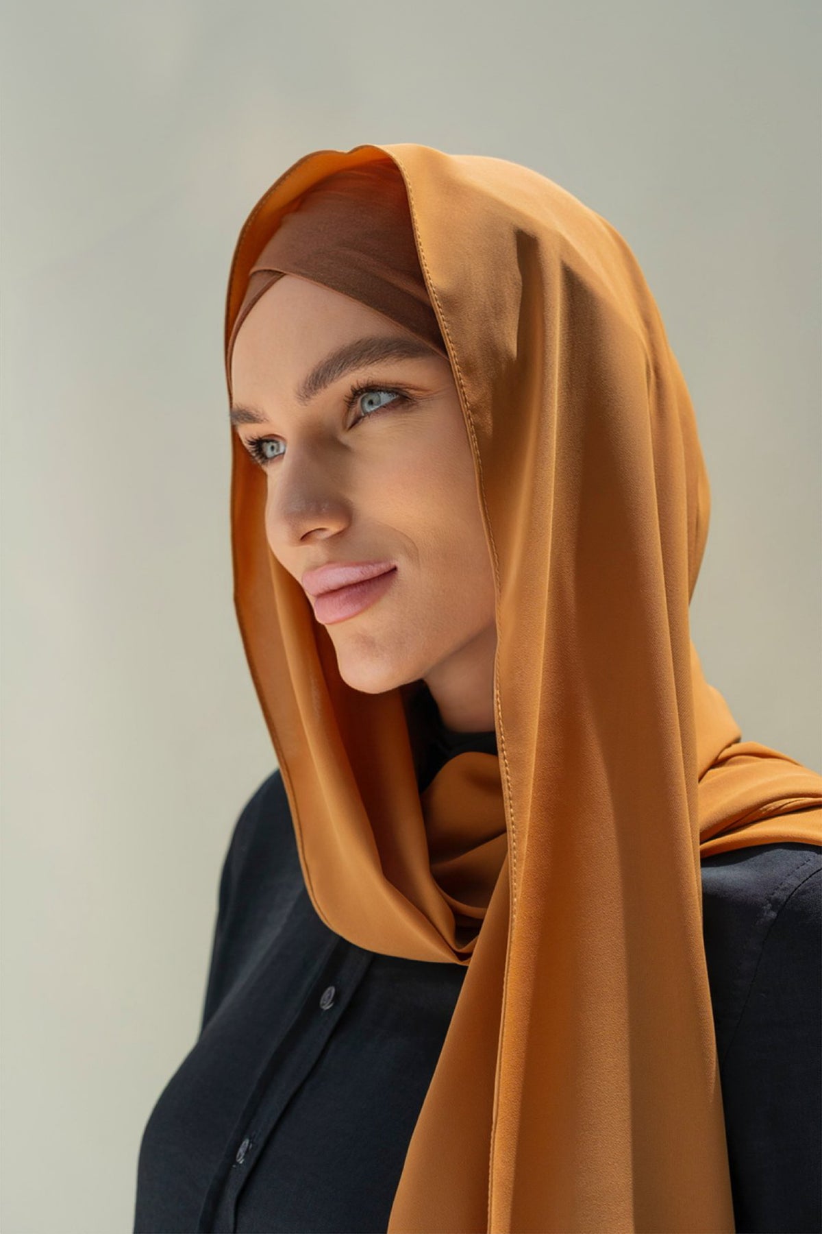 A woman wearing a brown scarf and inner cap, with a confident expression.