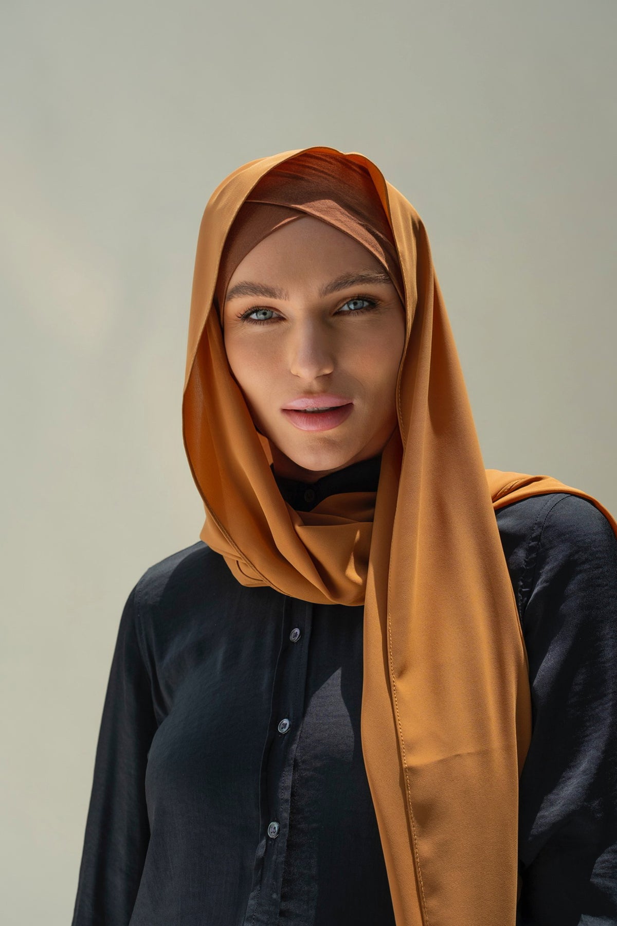 A woman wearing a brown scarf and inner cap, with a confident expression.