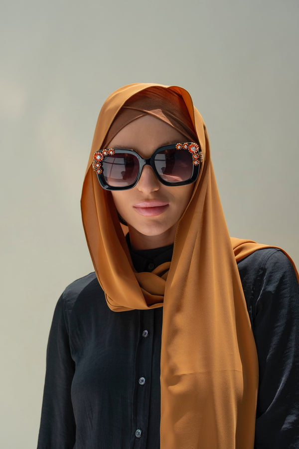 A woman wearing a brown scarf and inner cap, with a confident expression.