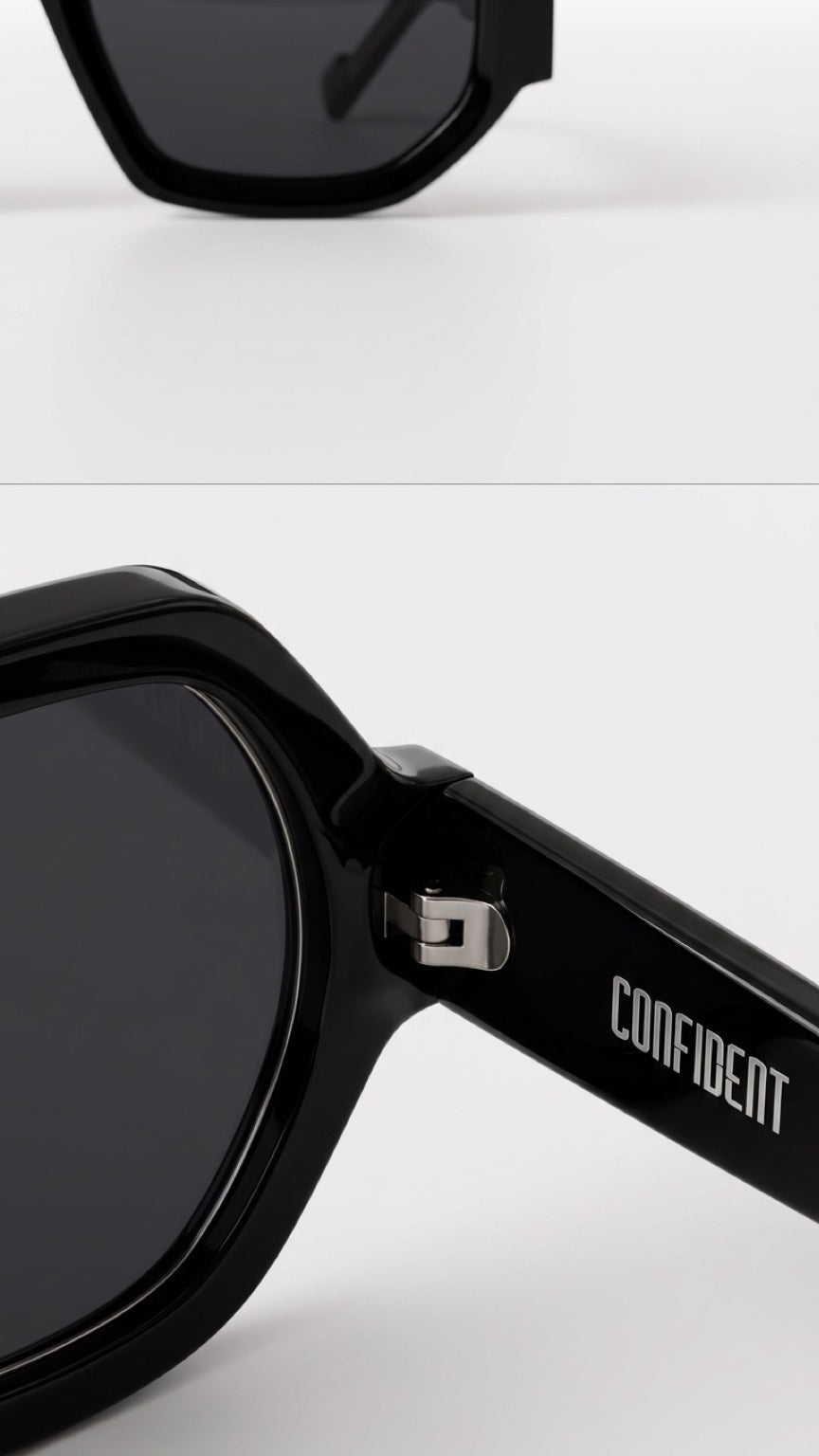 Close-up of black oversized sunglasses with dark lenses and a silver hinge, showing the brand name 'CONFIDENT' printed on the temple arm against a light gray background.