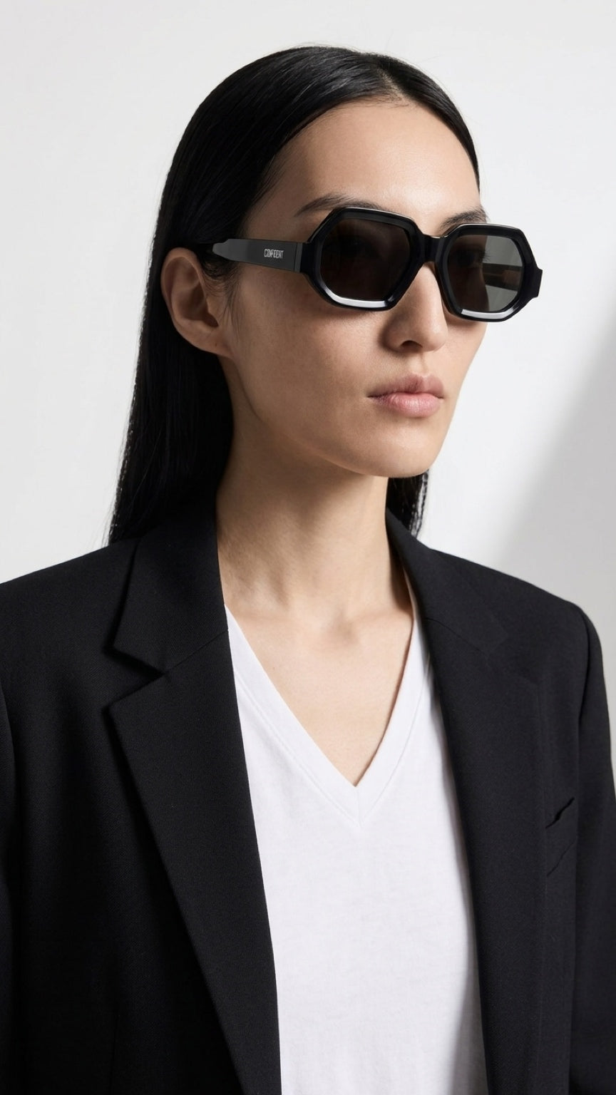 Woman wearing CONFILVARO black geometric sunglasses with dark lenses and a black blazer
