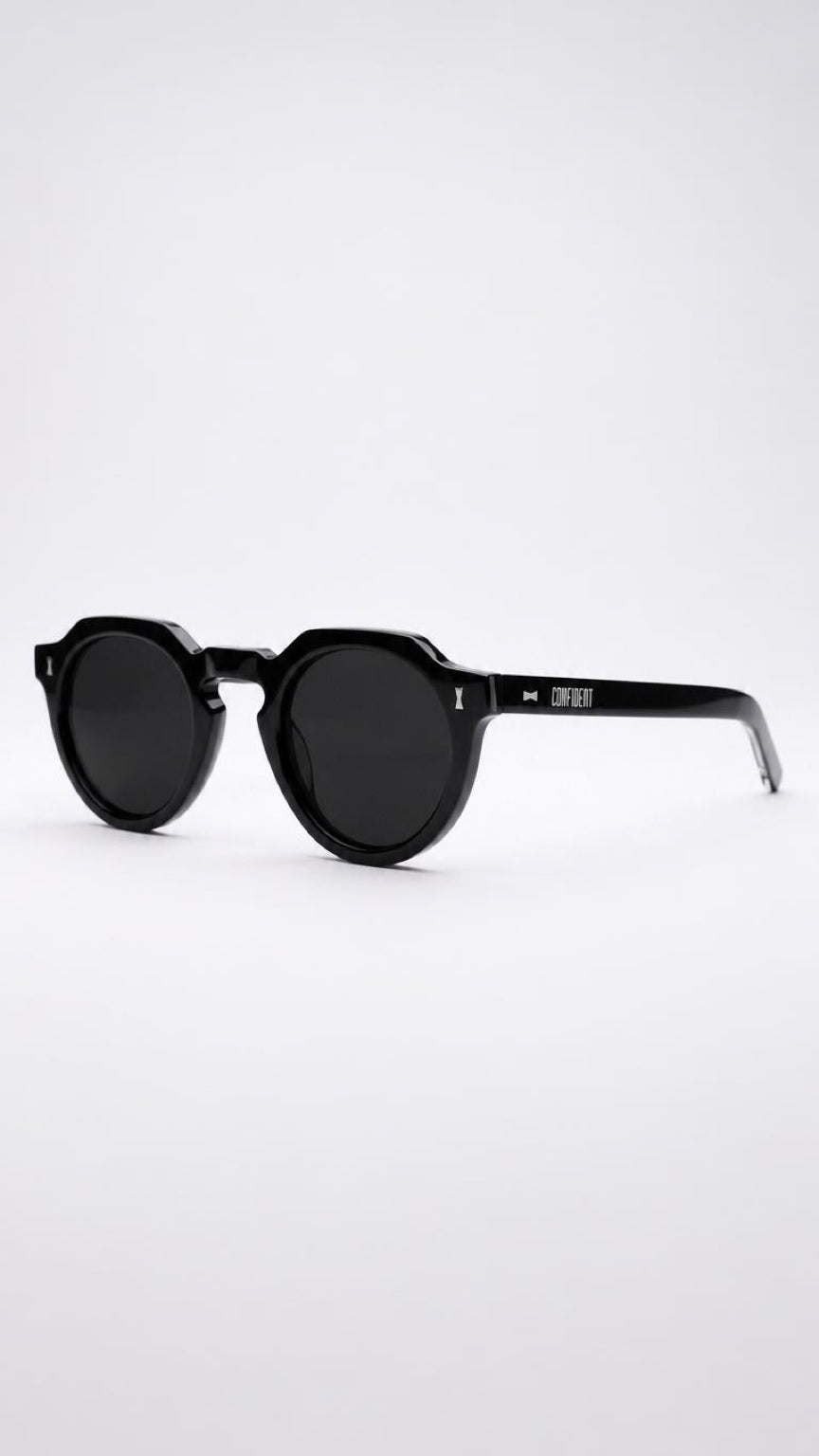 Black round-frame sunglasses with dark lenses and a confident  logo on the temple arm, photographed on a clean light gray background.