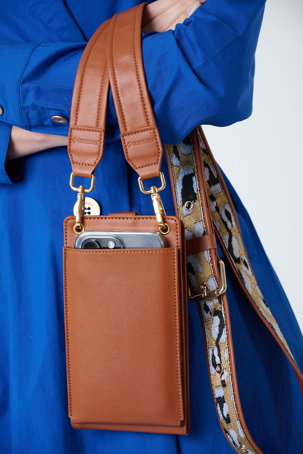 Model carrying CarryOn SunRise phone wallet bag in brown leather with gold strap”