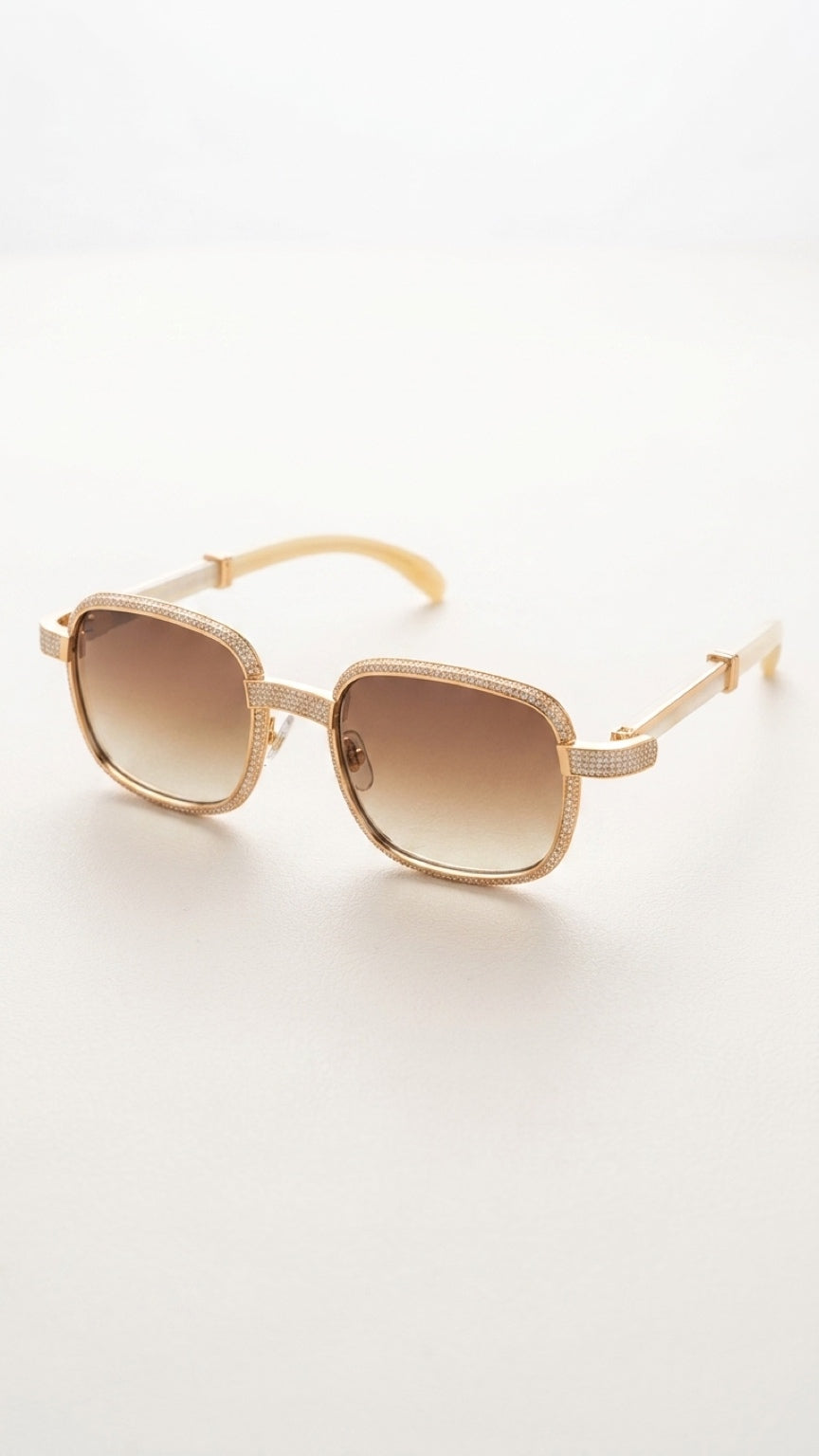 A pair of square sunglasses with a textured gold-tone frame and gradient brown lenses, resting on a clean white surface.