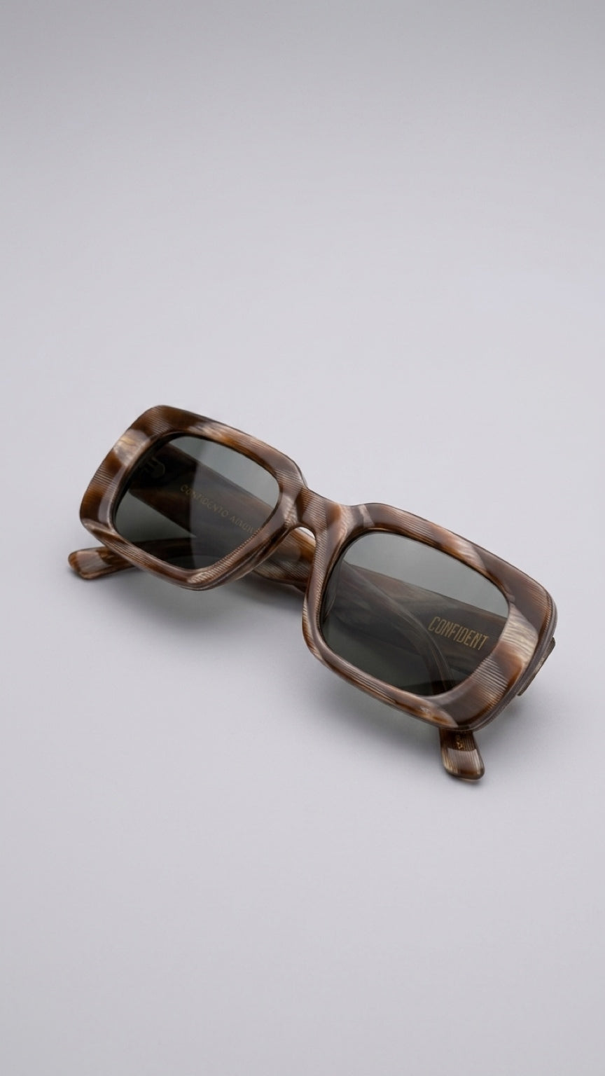 A pair of oversized square sunglasses with a glossy brown tortoiseshell frame and dark tinted lenses, displayed on a neutral light gray background.