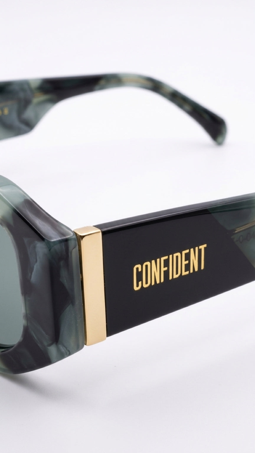 Close-up of square sunglassesCONFILVARO Sage Green Marble-Effect Rectangle Sunglasses with a black and green marbled acetate frame, gold metal bridge, and the brand name 'CONFIDENT' printed in gold on the temple arm.