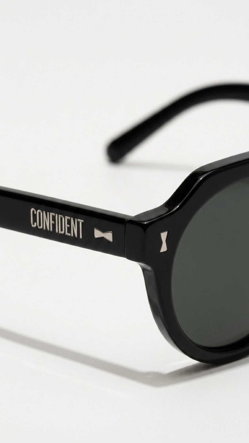 Close-up of a pair of black sunglasses with dark lenses, featuring the brand name 'CONFIDENT' printed in white on the temple arm, set against a clean white background.