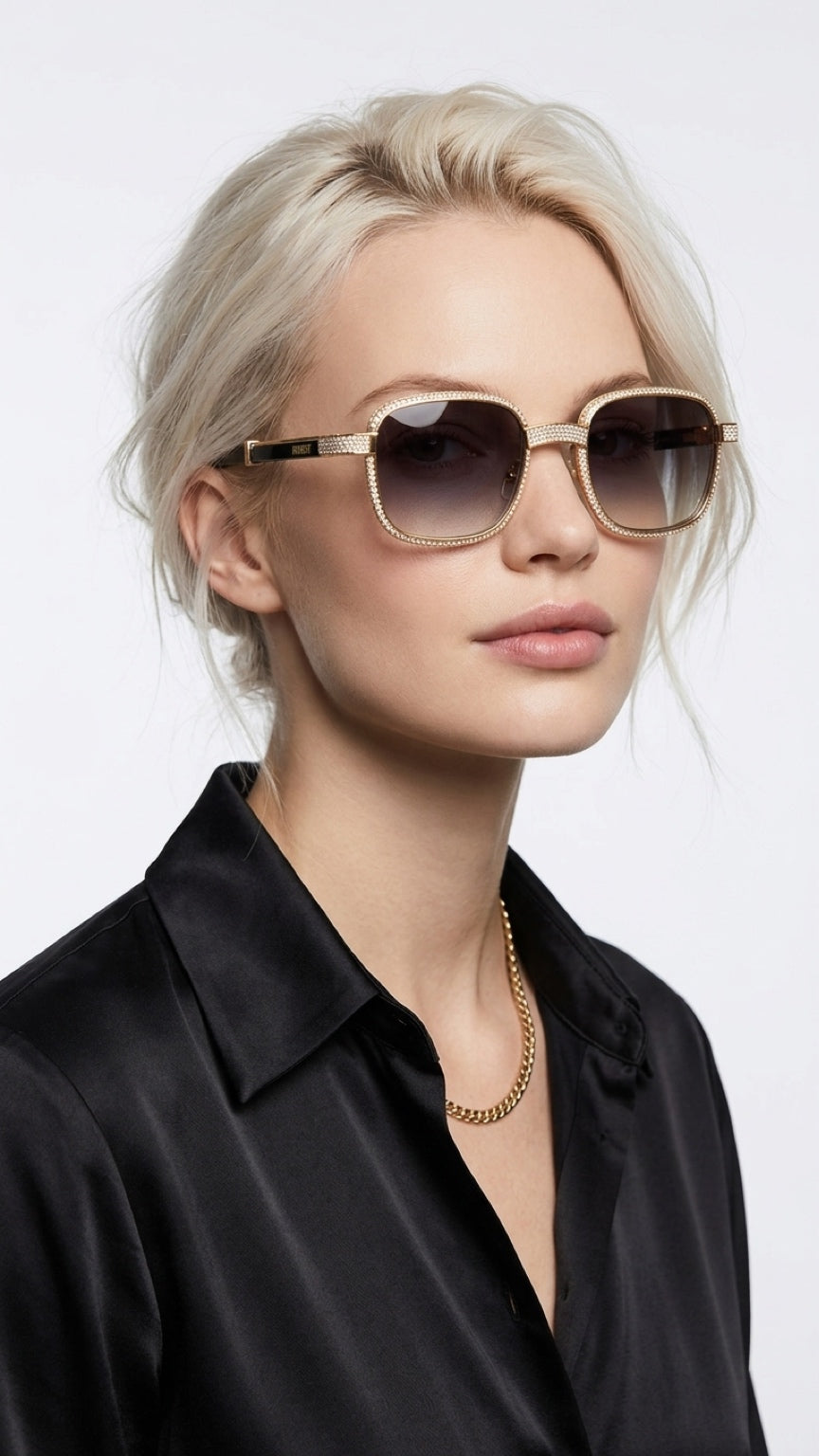 A blonde woman wearing square aviator-style sunglasses with gold metal frames and dark gradient lenses, paired with a black satin shirt and a gold chain necklace, against a light gray background.